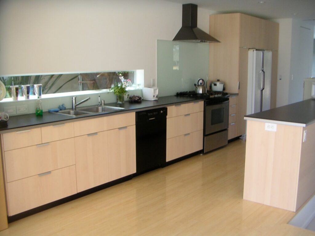 Contemporary kitchen with light wood cabinetry, long counter workspace, stainless appliances, and a horizontal window bringing in natural light.