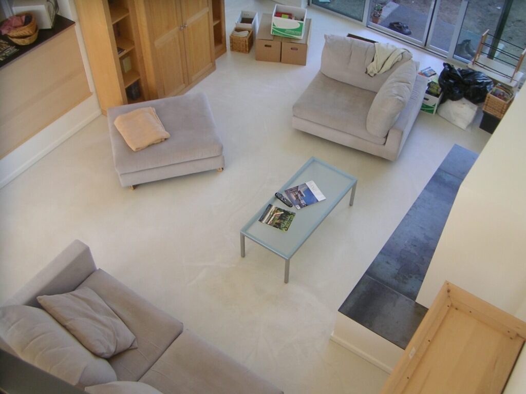 A modern living room viewed from above, featuring soft neutral furniture, built-ins, and full-height glass doors opening to the backyard.