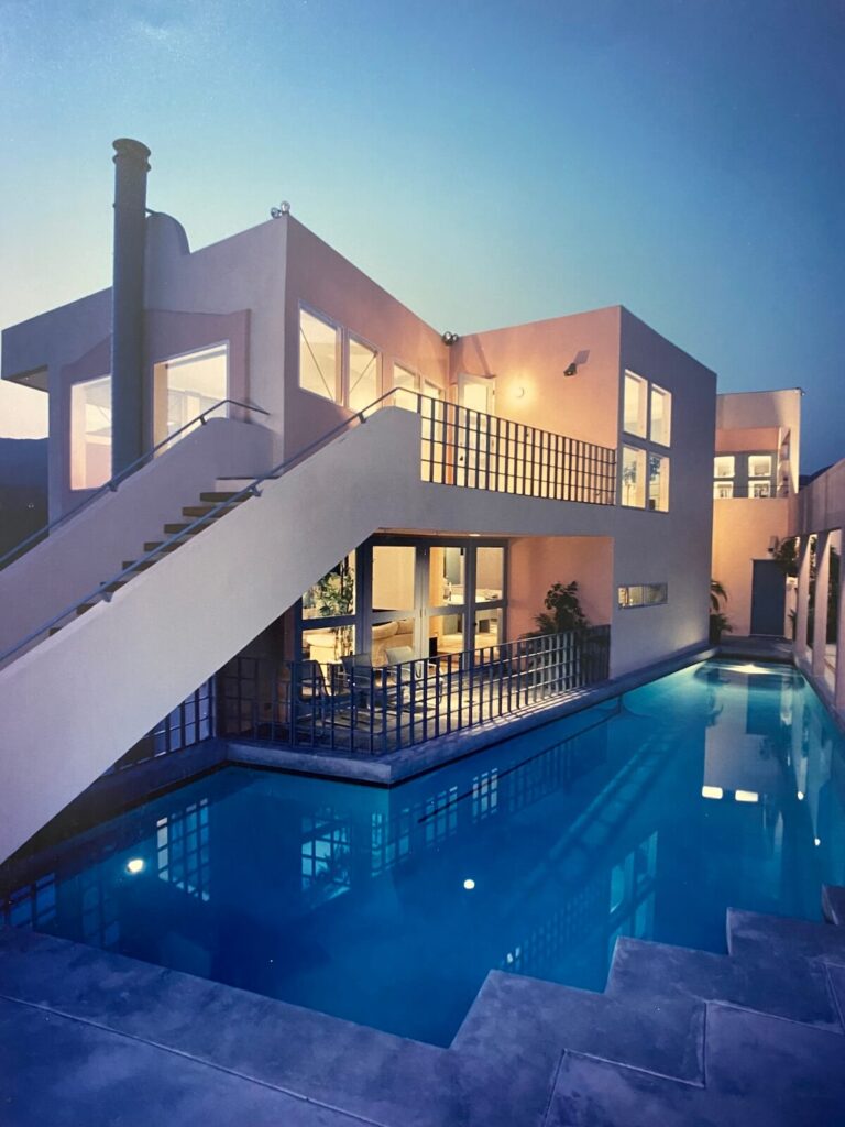 Twilight exterior of the Jacob Residence showcasing the elevated walkway, geometric railings, and long modern swimming pool designed by Richard Clemenson.