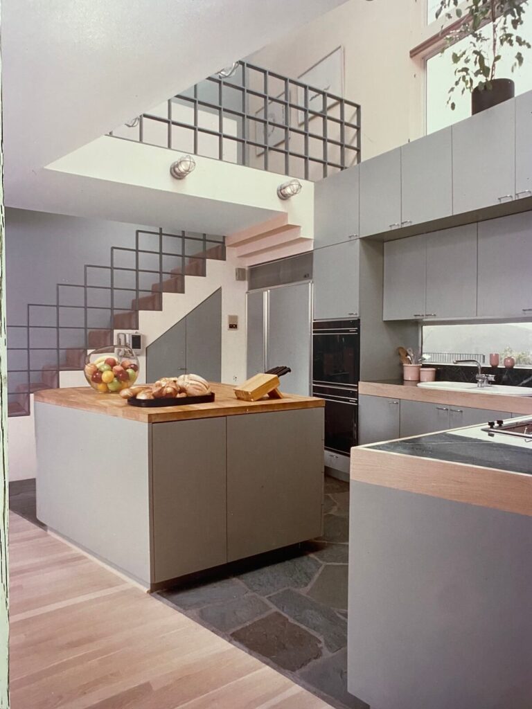 Contemporary kitchen at the Jacob Residence featuring a central island, geometric metal stair railing, and high clerestory windows designed by Richard Clemenson.