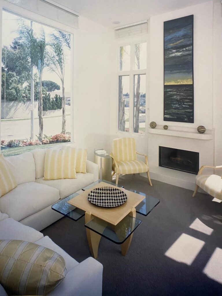 Bright living room at the Shore Residence featuring white sofas, yellow striped accents, tall windows, and a modern fireplace designed by architect Richard Clemenson.