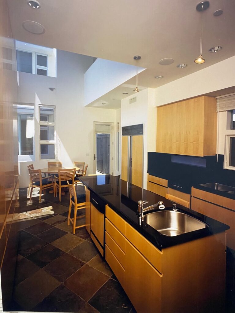 Modern kitchen at the Shore Residence with slate flooring, wood cabinetry, black stone countertops, and adjacent dining area architecture by Richard Clemenson.