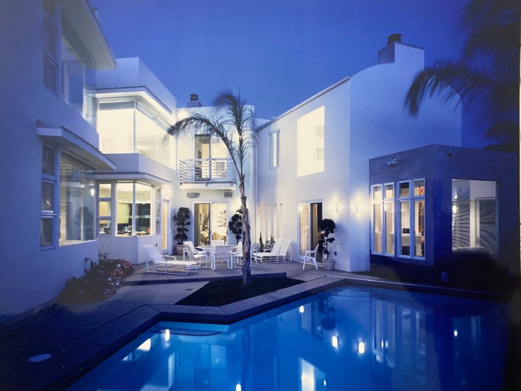 Evening view of the Shore Residence courtyard in Seal Beach, featuring glowing interior spaces, a landscaped patio, and a reflecting pool.