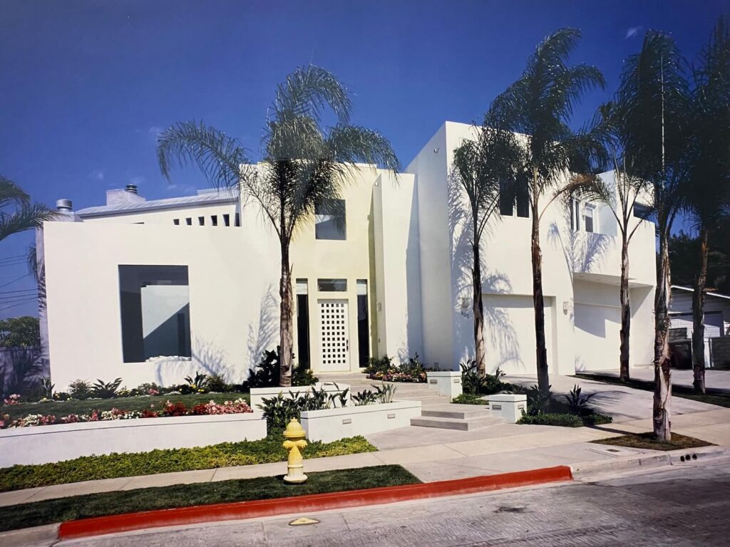 Front façade of the Shore Residence in Seal Beach, with modern white geometric forms, palm trees, and a landscaped entrance.