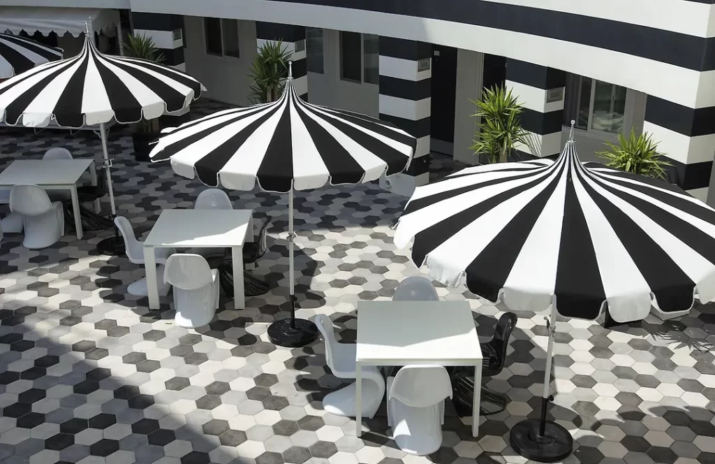Black-and-white striped umbrellas in the courtyard of The Carlyle Inn in West Los Angeles over patterned tile flooring.